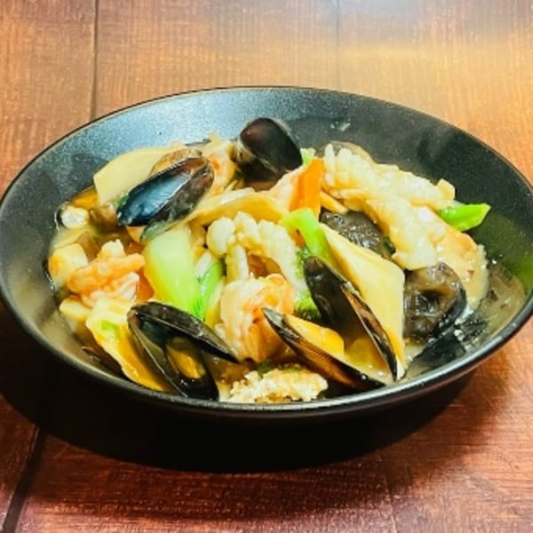 A black bowl of Man Chun Hong seafood stir-fry with mussels, shrimp, squid, and vegetables.