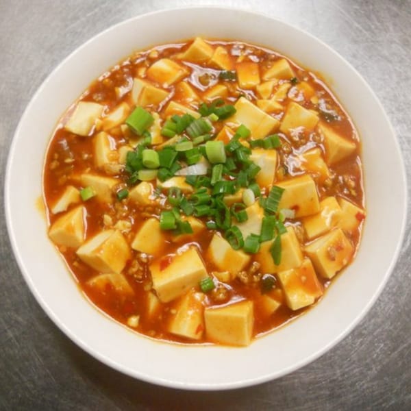 Man Chun Hong's Mapo Tofu, a Chinese dish with tofu cubes in spicy red sauce, garnished with green onions.